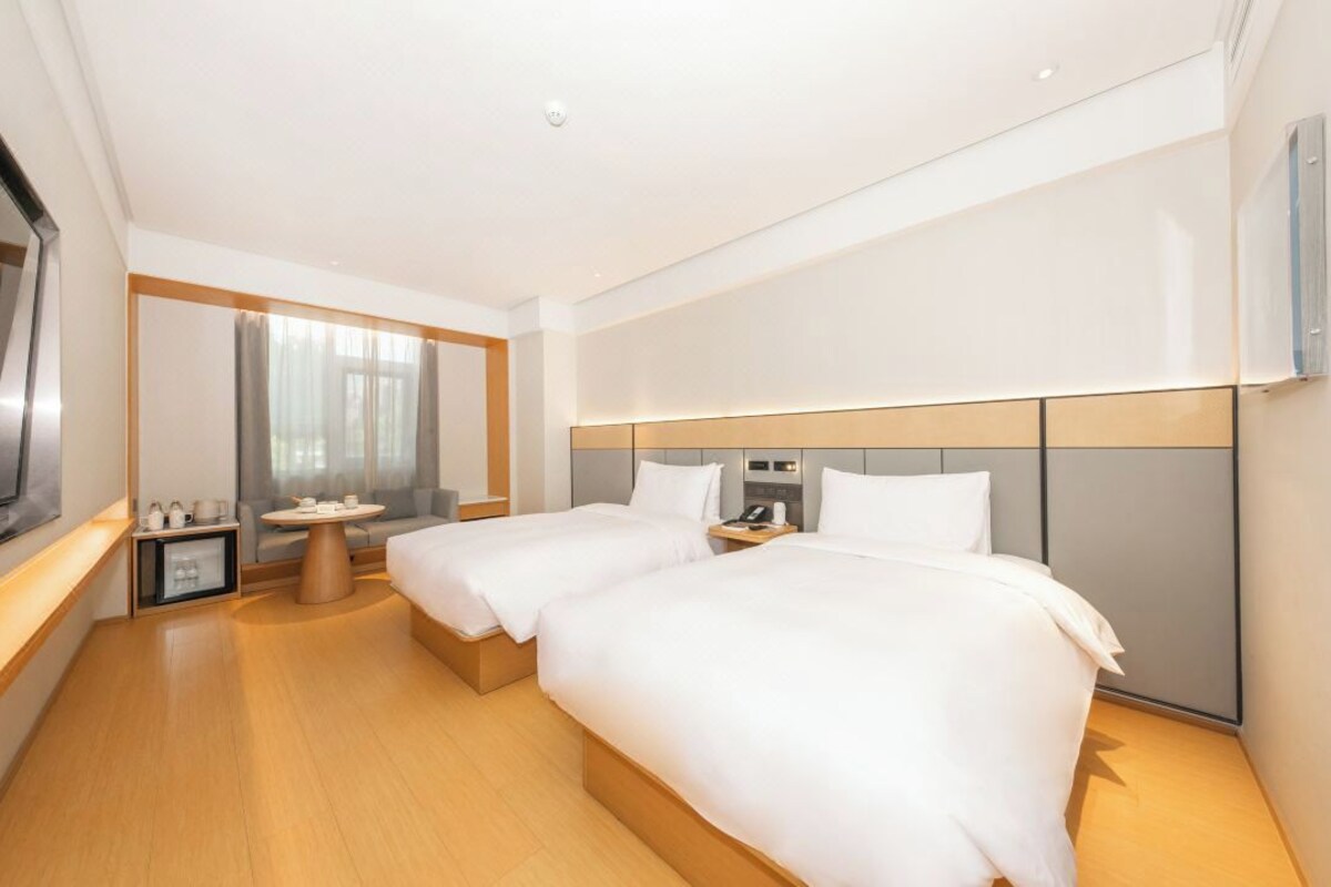 Habitación de hotel con dos camas, una mesita, un televisor y un espejo.