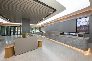 Um hall de hotel moderno com balcão de recepção, área de estar e um grande painel digital.