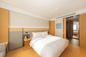 Una habitación de hotel moderna con una cama grande, una mesita de noche con un teléfono y una taza, un televisor montado en la pared y una puerta que da a otra habitación.