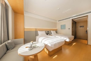 A hotel room with a sofa, a round table, two beds, a wooden headboard, and a door leading to another room. - Ji Hotel Gu An Daxing International Airport (Langfang)