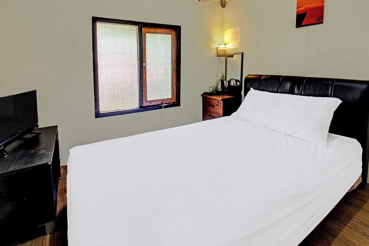 Habitación de hotel con cama, televisor, mesita de noche, lámpara, ventana y una obra de arte en la pared.