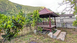A wooden gazebo with a tiled roof, surrounded by lush greenery and a hillside in the background. - Oyo 91830 Hotel Gemilang 2 (Sembalun Lawang)