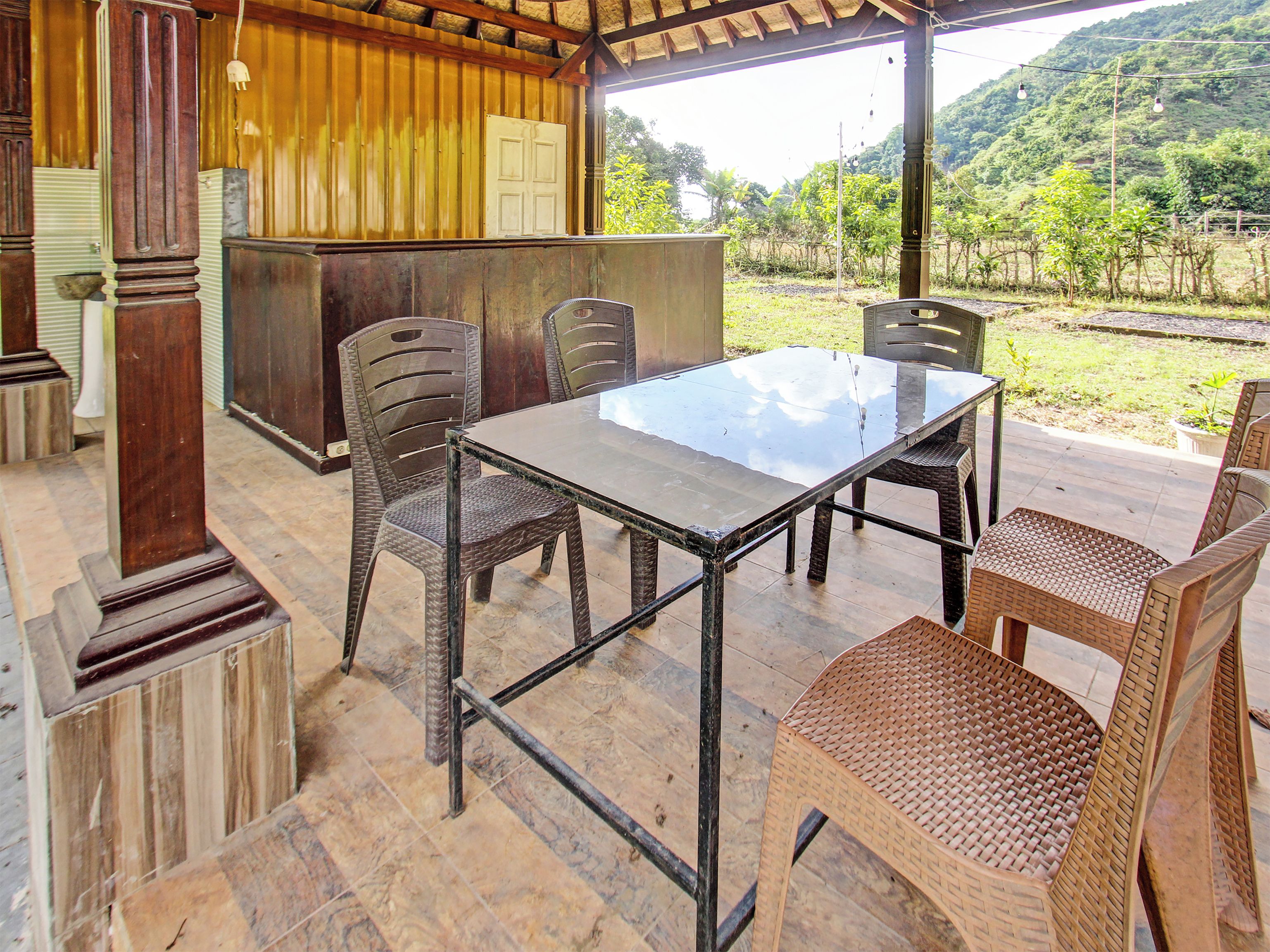 An outdoor patio with a glass-top table, wicker chairs, and a wooden structure with a door.