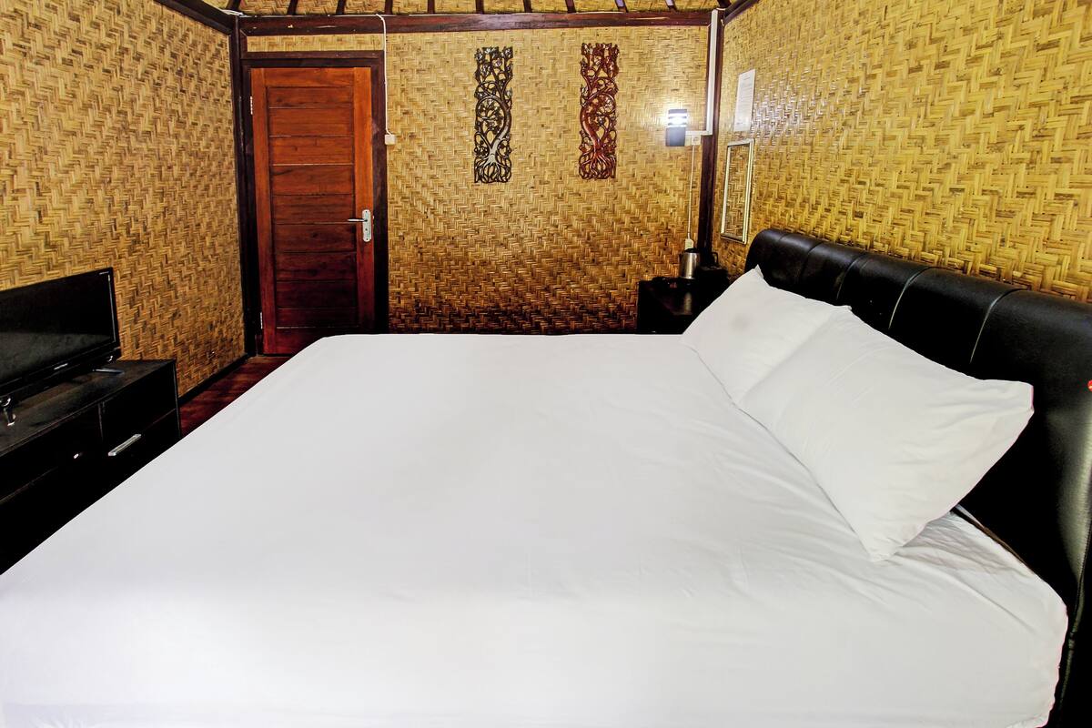 Una habitación con una cama, una puerta de madera, una lámpara de pared y un televisor sobre un mueble.
