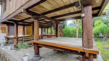 An outdoor wooden structure with a covered seating area, columns, and potted plants.