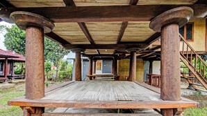 Um deck de madeira coberto com colunas, um banco e uma escadaria que leva a um edifício.