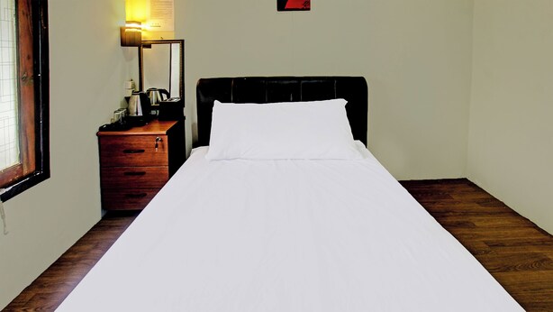 A single bed with white bedding in a room with a wooden floor, a wooden nightstand with a lamp, and a mirror on the wall. - Oyo 91830 Hotel Gemilang 2 (Sembalun Lawang)
