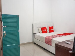 Una camera d'albergo con un letto, un armadio color petrolio e un comodino con un telecomando.
