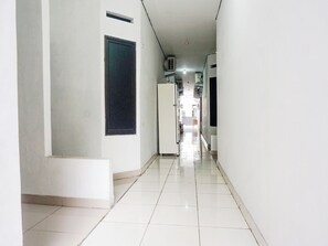Een gang met witte wanden en betegelde vloer, die leidt naar een kamer met raam en deur.