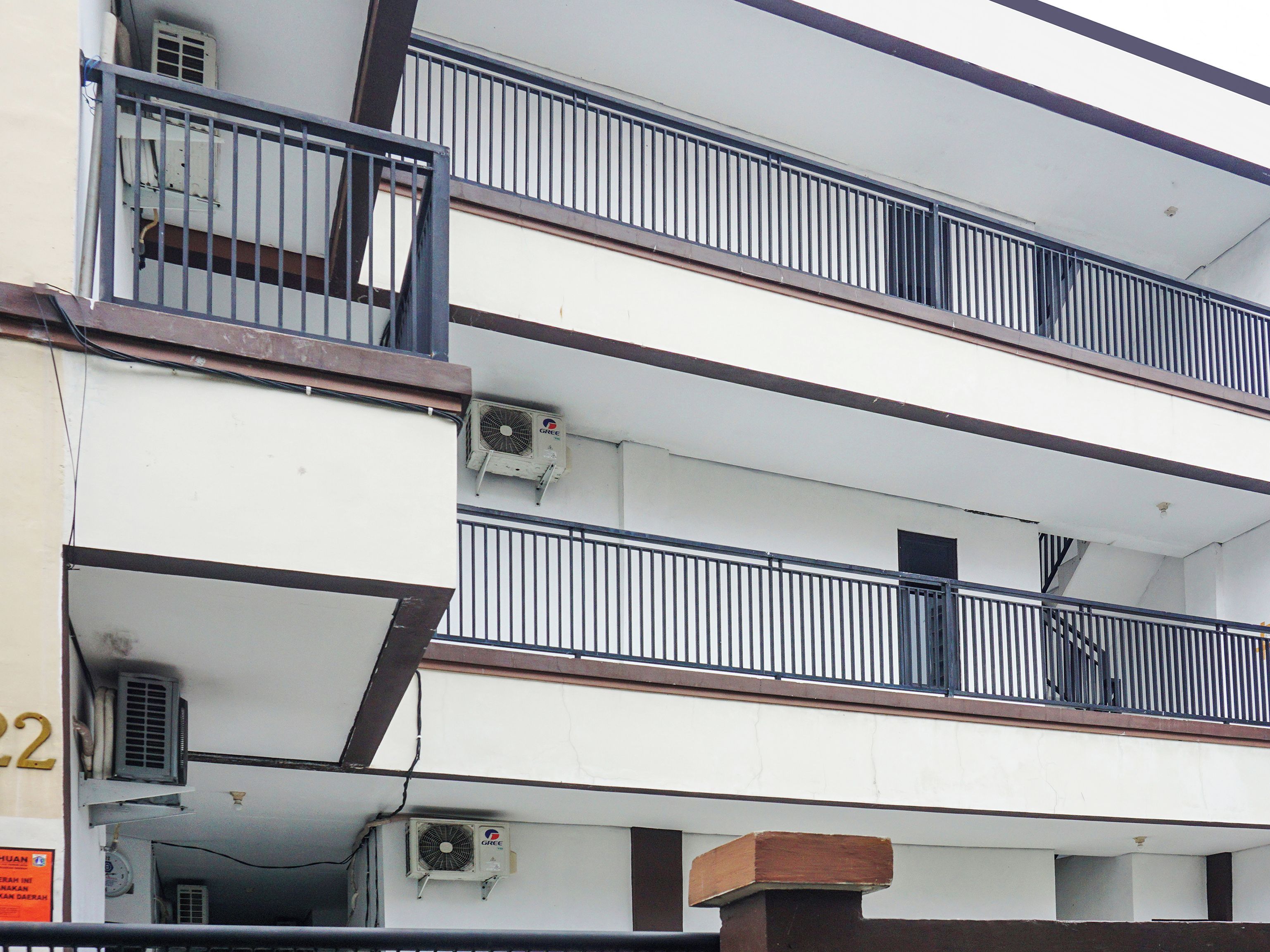 A multi-story building with balconies, air conditioning units, and a visible sign with text.