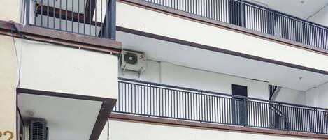 A multi-story building with balconies, air conditioning units, and a visible sign with text.