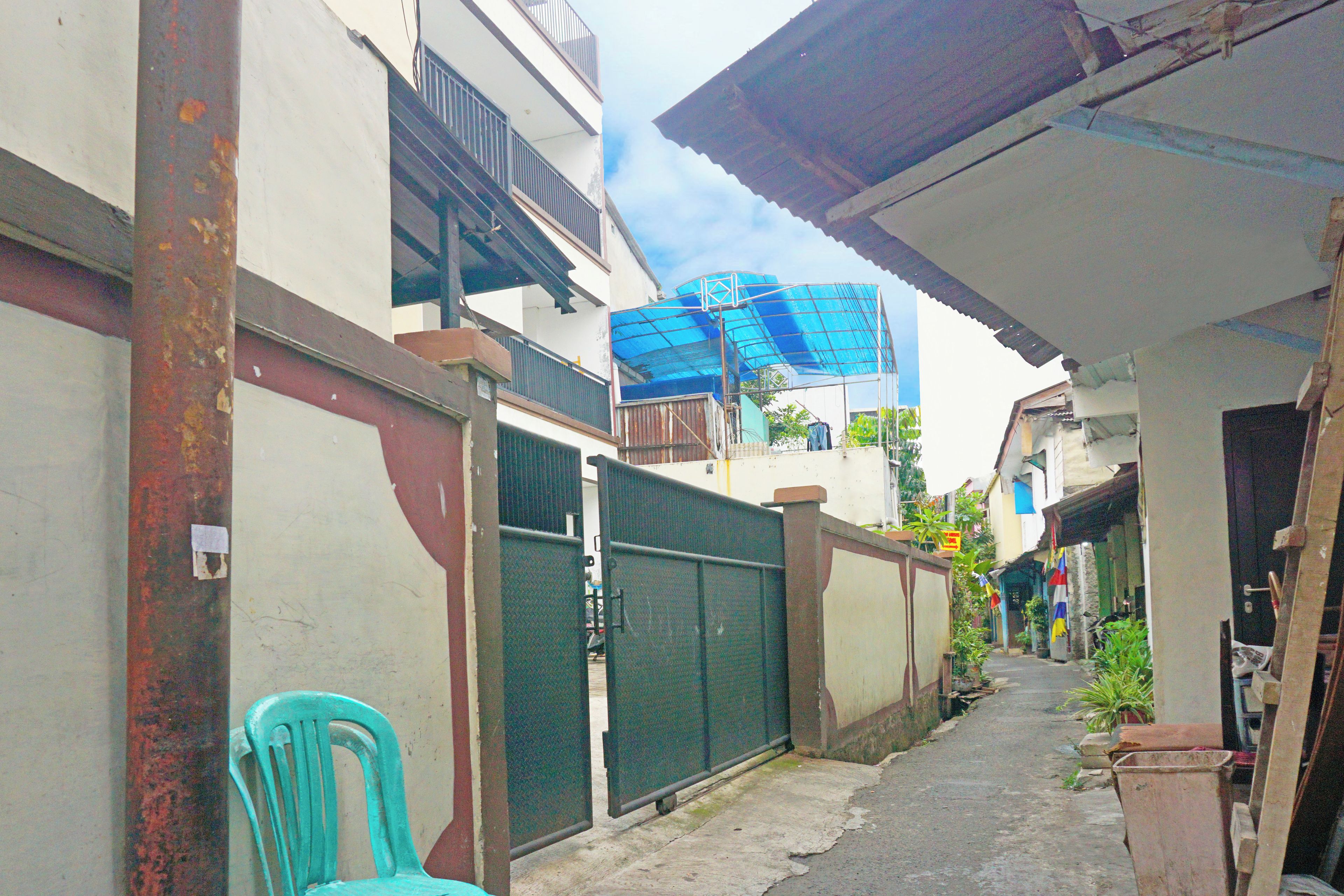 A narrow alleyway with a metal gate, a blue tarp, and a green chair.