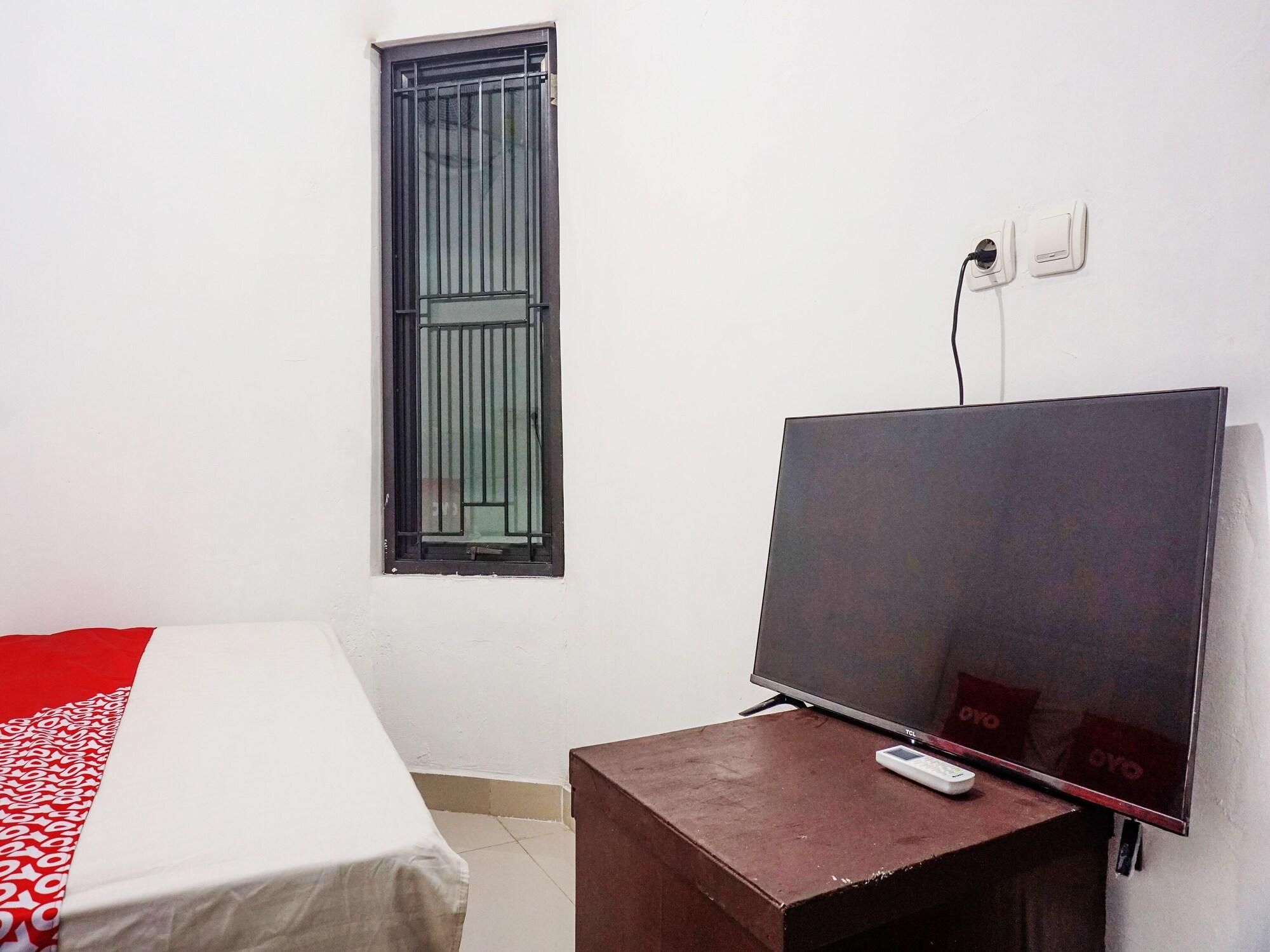 A room with a bed, a TV on a stand, a window with metal bars, and a power outlet.
