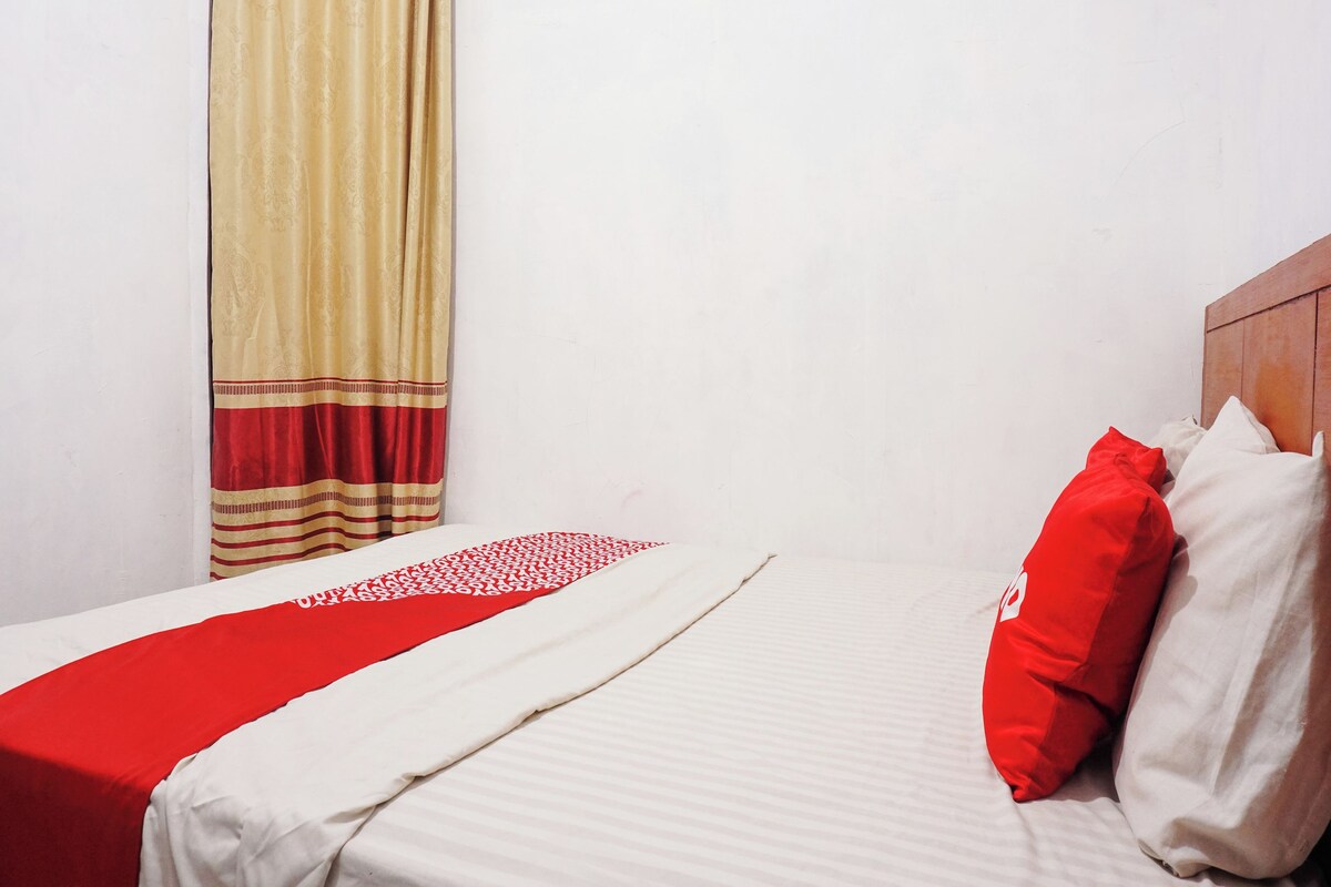 Un letto rifatto con cura, con una coperta a righe rosse e bianche, una testiera in legno e una finestra con tende color beige.