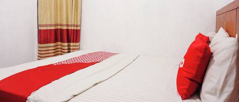 A neatly made bed with a red and white bedspread, a wooden headboard, and a window with beige curtains.