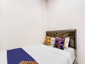 Una cama con colcha blanca y azul, cabecera marrón y tres almohadas decorativas con diseños geométricos.