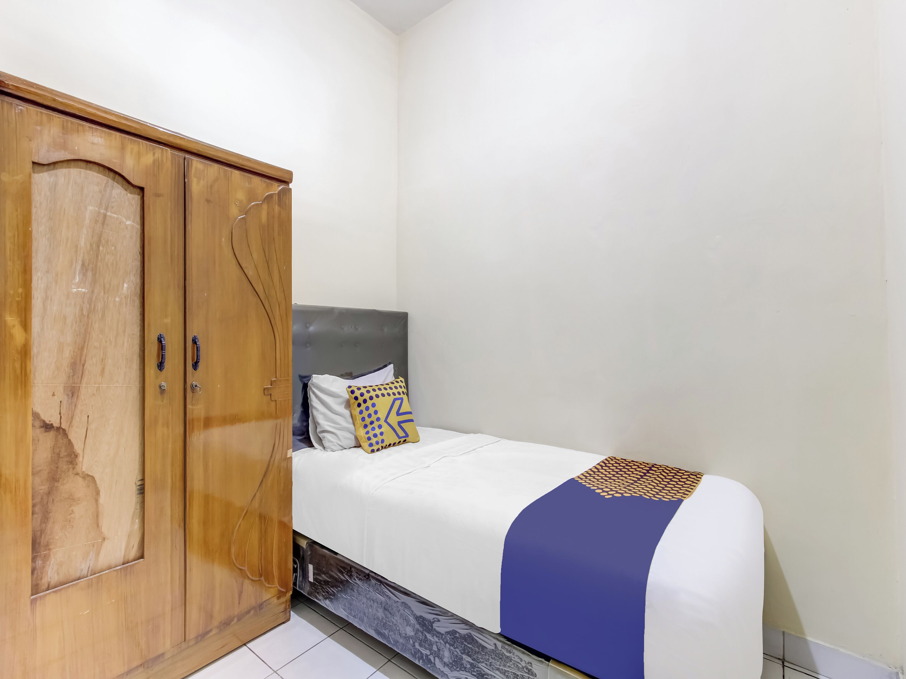 A bedroom with a bed, a wooden wardrobe, and a grey headboard.