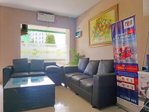 Uma área de recepção com sofá, cadeiras, mesa de vidro, um cartaz e uma janela com persianas.