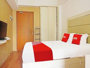 Quarto de hotel com cama, guarda-roupa, televisão e mesa de cabeceira.