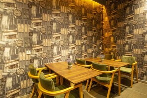 A dining area with a wall of clocks and vintage-style posters, a wooden table, and green upholstered chairs. - Taksim Leon S Hotel (Istanbul)