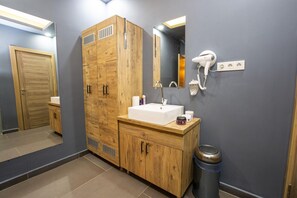 A bathroom with wooden cabinets, a sink, a mirror, a hairdryer, and a trash bin. - Taksim Leon S Hotel (Istanbul)