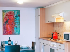A compact kitchen with white cabinets, a microwave, a red kettle, and a dining table with chairs. - Apartment  by Interhome (Zurich)