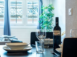 A dining table with a bottle of wine, a glass, and plates, set against a window with a view of a building. - Apartment  by Interhome (Zurich)