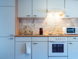 A modern kitchen with white cabinets, a built-in microwave, a stove, and a red electric kettle. - Apartment  by Interhome (Zurich)