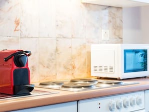 Une cuisine avec une machine à café rouge, un four à micro-ondes blanc et une cuisinière.
