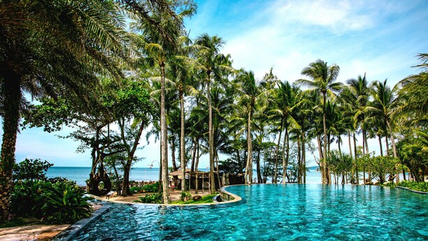 A clear blue infinity pool surrounded by palm trees and a view of the ocean. - Ocean Bay Resort & Spa Phu Quoc (Phu Quoc)