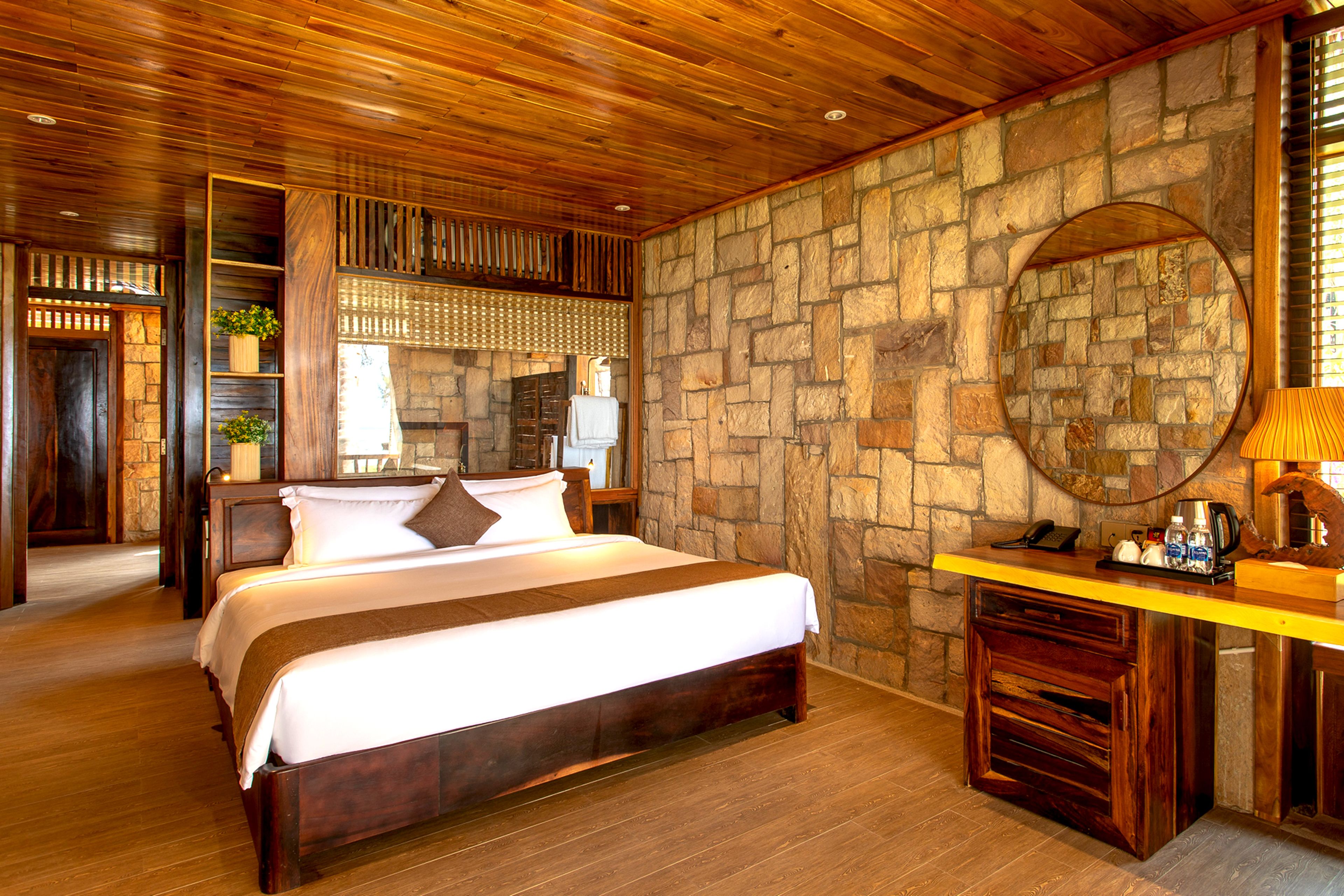 A wooden-paneled bedroom with a stone wall, a bed, a nightstand, and a mirror.