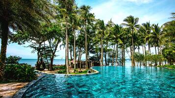 A clear blue infinity pool surrounded by palm trees and a view of the ocean.