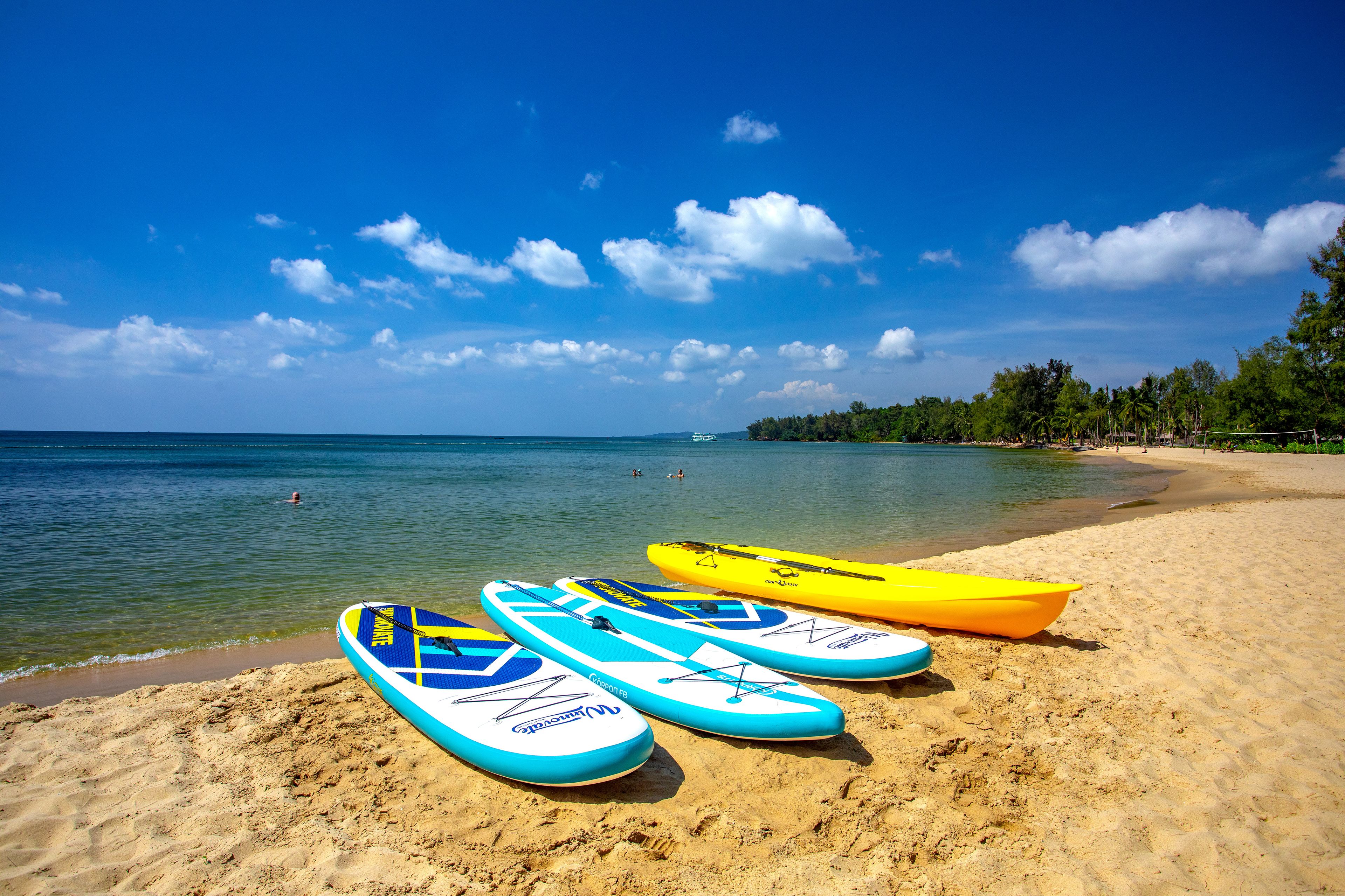 A beach with three kayaks on the sand and a clear blue sky.