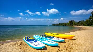 A beach with three kayaks on the sand and a clear blue sky.