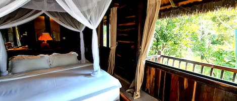 A bed with a canopy, a nightstand with a lamp, and a view of greenery outside.
