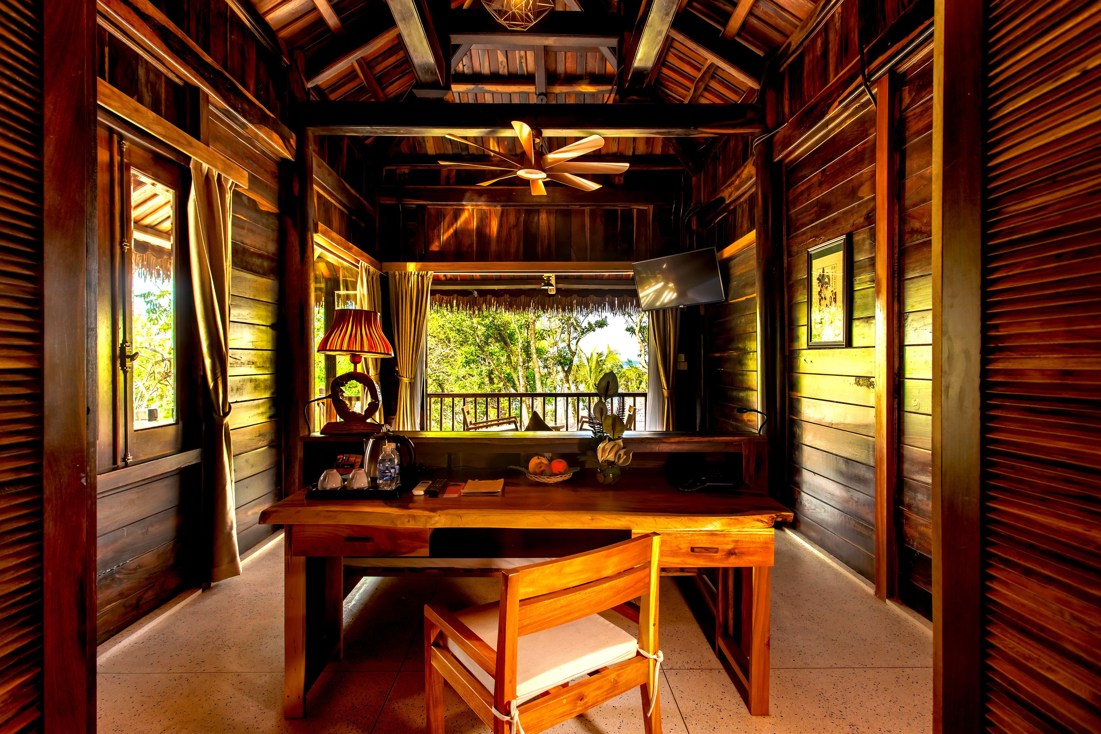 A wooden interior with a table, chairs, a ceiling fan, a window with curtains, and a framed picture on the wall.