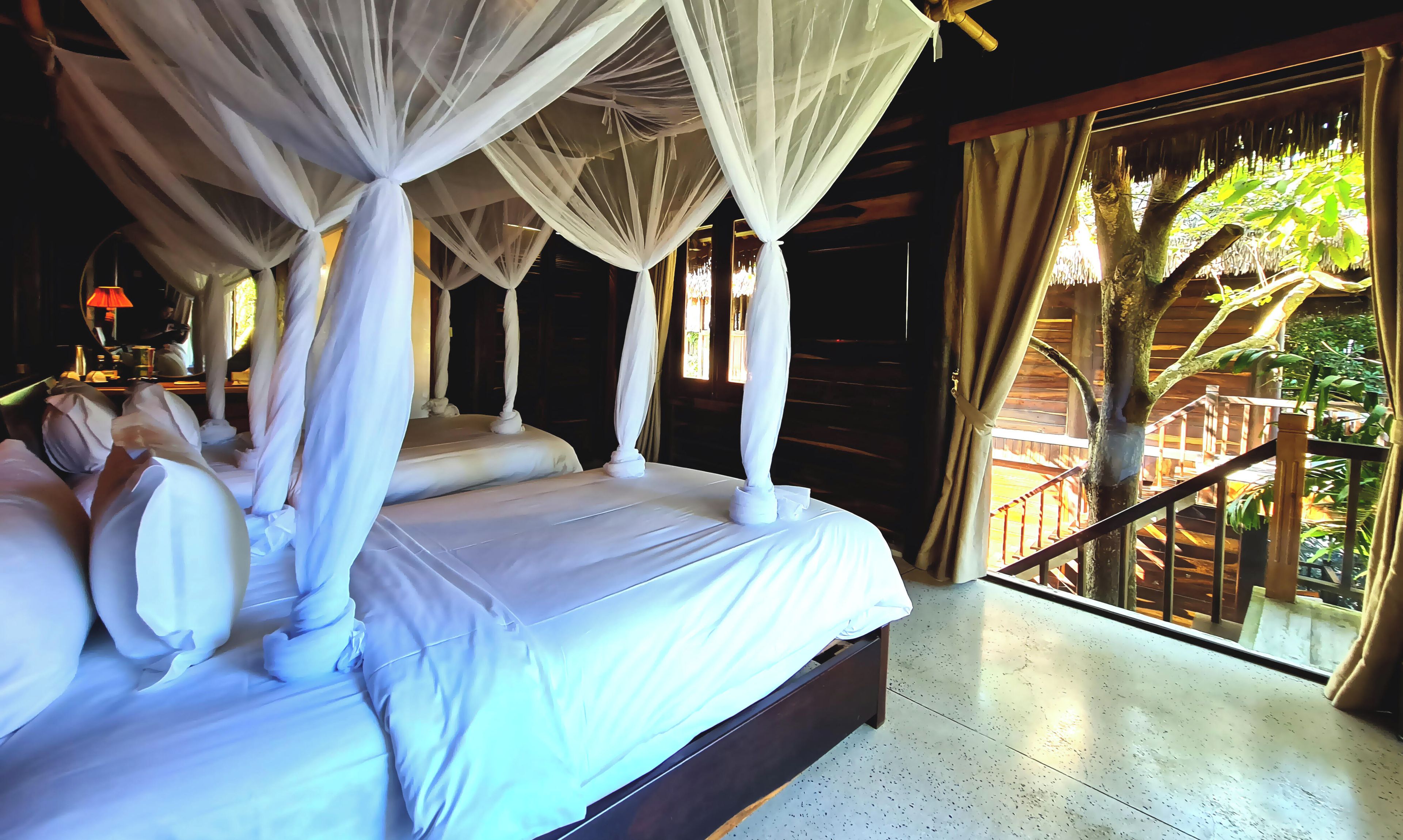 A four-poster bed with a canopy, a wooden floor, and a view of a wooden deck and trees.