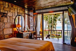 A bedroom with a large bed, a desk with a lamp, a chair, and a view of the ocean through a sliding glass door. - Ocean Bay Resort & Spa Phu Quoc (Phu Quoc)