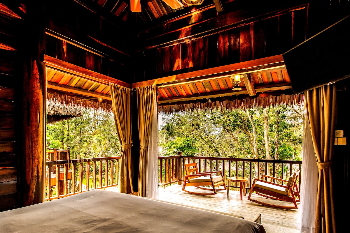 A wooden cabin with a balcony, a bed, and rocking chairs.