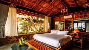 A wooden-framed bedroom with a large bed, a small table with a plant, and a view of greenery outside. - Ocean Bay Resort & Spa Phu Quoc (Phu Quoc)