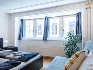 Ein modernes Schlafzimmer mit einem Bett, Nachttischen, einem Heizkörper und einem großen Fenster mit Vorhängen.