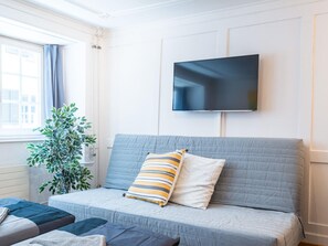 A modern living room with a grey sofa, a flat-screen TV mounted on the wall, and a potted plant. - Apartment  by Interhome (Zurich)