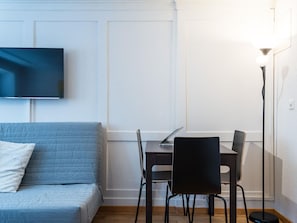 A modern living room with a flat-screen TV mounted on the wall, a sofa, a dining table with chairs, and a floor lamp. - Apartment  by Interhome (Zurich)