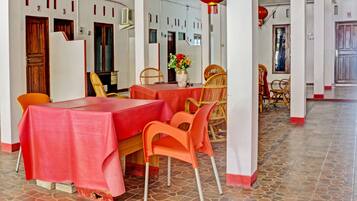Un comedor con una mesa roja, sillas anaranjadas y un jarrón con flores.