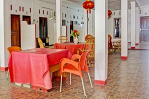 Un comedor con una mesa roja, sillas anaranjadas y un jarrón con flores.
