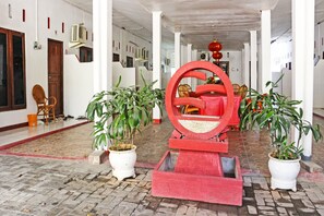 A corridor with potted plants, a red circular structure, and a wooden door. - Oyo 91416 Puri 88 Homestay (Kupang)