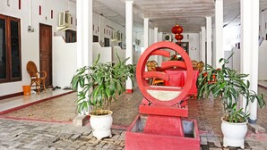 Un couloir orné de plantes en pot, une structure circulaire rouge et une porte en bois.