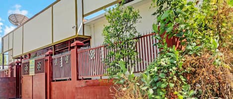 A gated residential area with a satellite dish, a red fence, and overgrown vegetation.