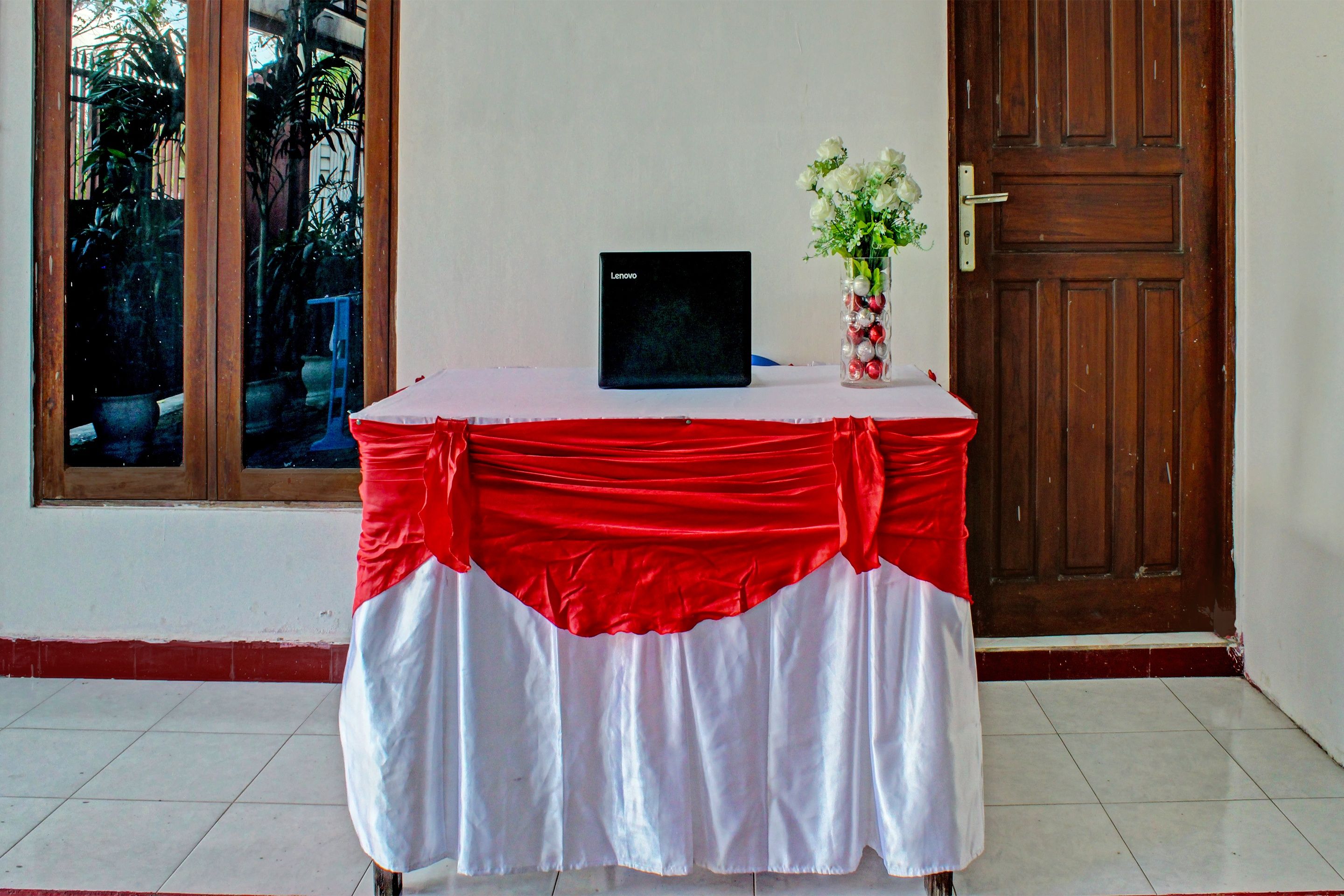 Ein Tisch mit einem Laptop, einer Blumenvase und einer rot-weißen Tischdecke.