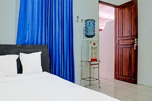 A hotel room with a bed, blue curtains, a water dispenser, a wooden door, and a tiled floor. - Oyo 91416 Puri 88 Homestay (Kupang)